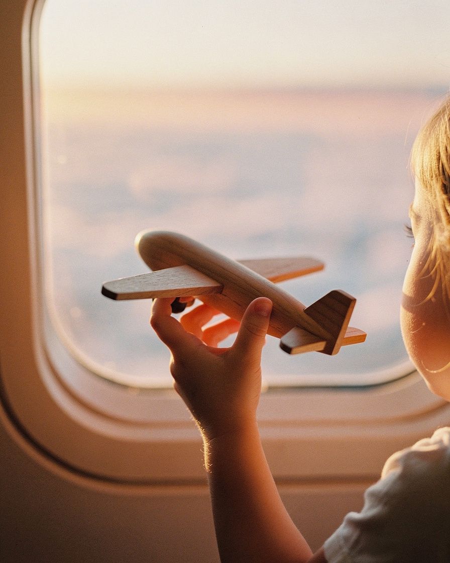 A child's hand holding a wooden toy against an aircraft window at sunrise